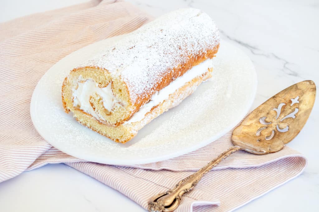 Swiss roll on a white plate with a serving spoon and tea towel. 