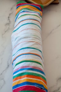 A colorful striped Swiss Roll bolster cushion on a marble surface.