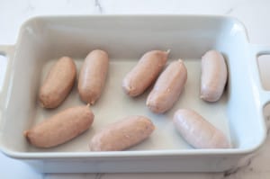 Raw sausages arranged in a ceramic baking dish for toad in a hole.