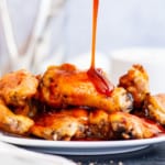 A plate of spicy Sriracha wings with sauce being poured on top.