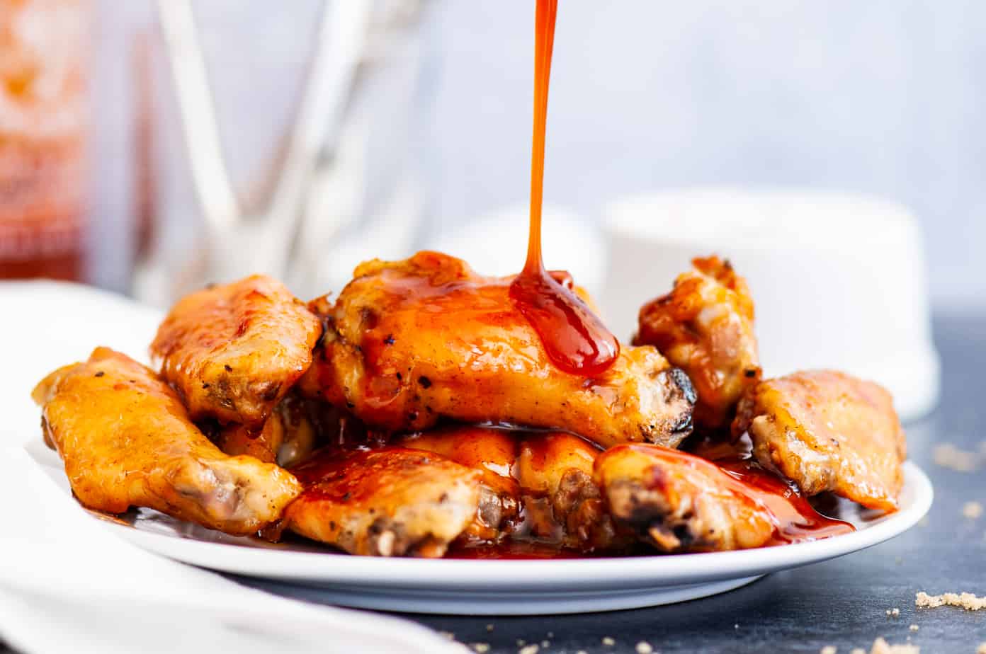 A plate of spicy Sriracha wings with sauce being poured on top.