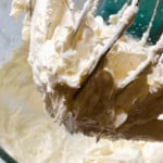 Whisk attachments lifting creamy, whipped mixture from a glass bowl, working towards a semi-homemade buttercream recipe.