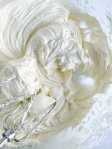 Whipped cream at a soft peak stage being mixed in a bowl for gingerbread cinnamon rolls.