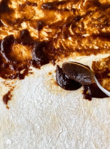 A spoon spreading the filling onto dough for gingerbread cinnamon rolls.