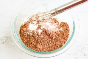 Mixing dry ingredients for Instant Pot Brownie Bites in a glass bowl with a whisk.