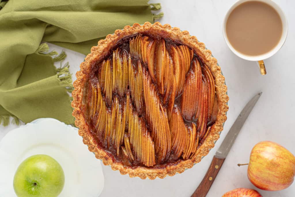 Overhead view of a freshly baked easy apple tart next to a cup of coffee, with whole apples and a knife on the side.