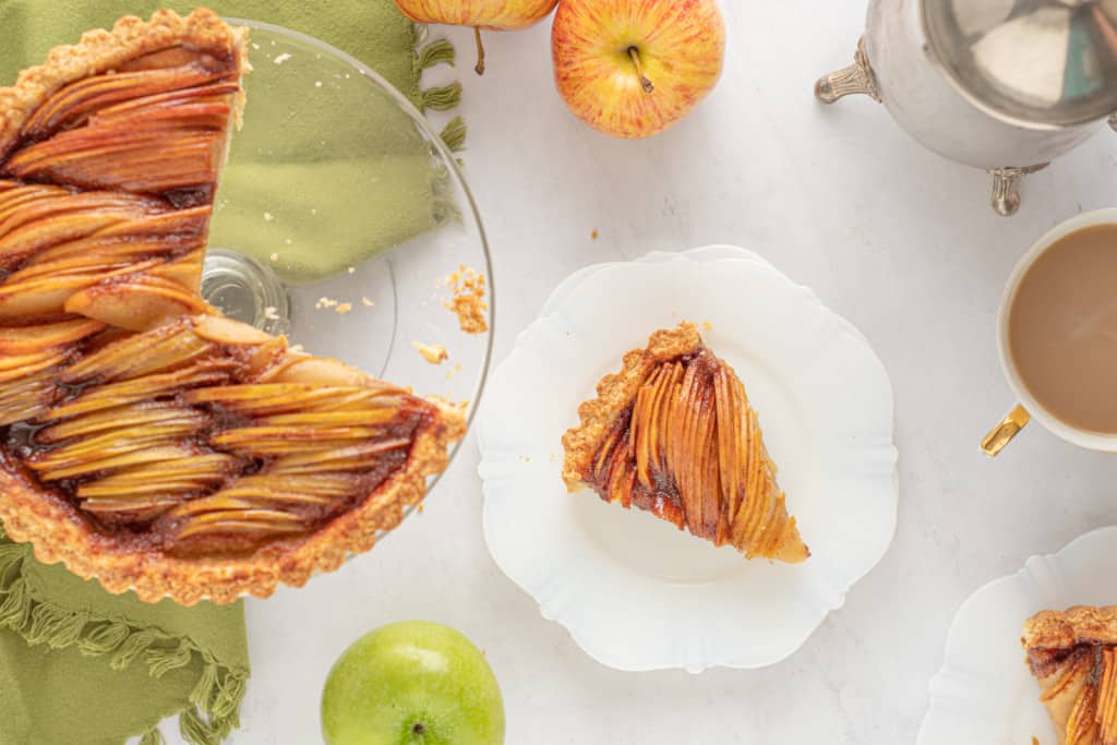 Sliced apple tart served with coffee on a white table.