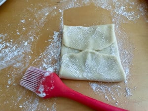 Folded filo dough and cornstarch scattered across the counter, with a silicone brush nearby.