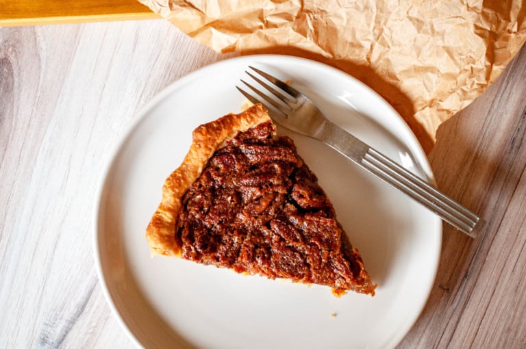 A slice of maple pecan pie in a white plate with fork on the side.