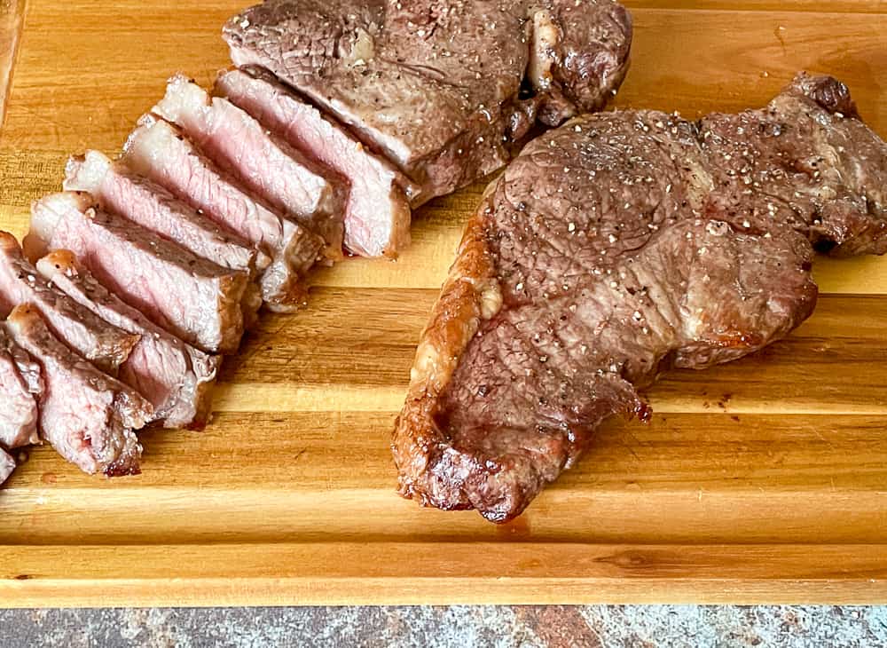 Two air-fried steaks with one sliced into strips revealing a medium-rare interior, and the other steak whole.