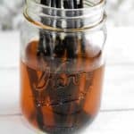 A jar filled with vanilla extract with vanilla beans immersed inside.
