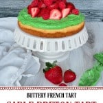 A green-frosted Sablé Breton tart topped with fresh strawberries sits on a white cake stand; two strawberries rest beside it. Text below describes it as a Sable Breton Tart with a shortbread crust.