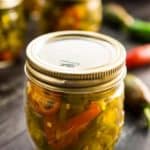 A jar of sliced candied jalapeños, also known as cowboy candy, with more of it in the background.
