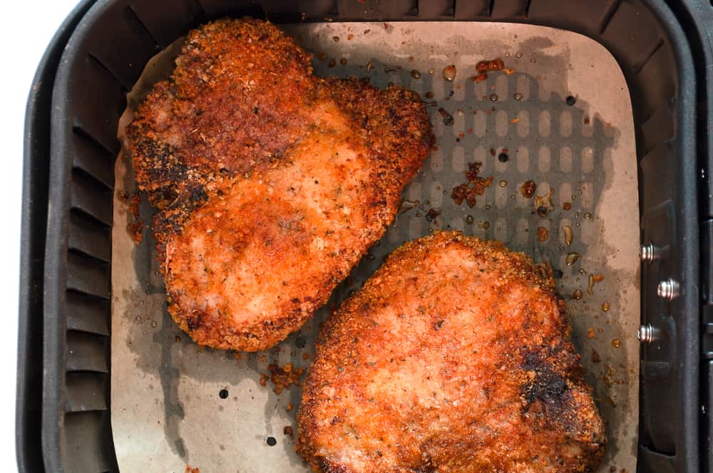 Two cripsy baked air fryer chops IN the air fryer basket. 