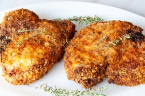 Crispy air fryer pork chops served on a white plate with thyme leavesf for garnish.