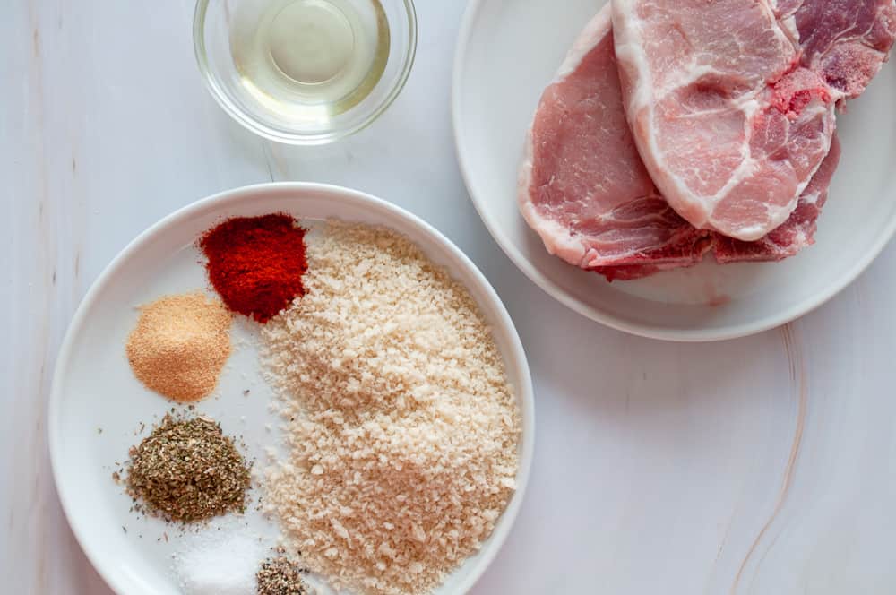 Ingredients for air fryer pork chops, oil, panko, spices, herbs, chops, and oil.
