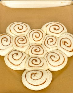 Cinnamon rolls arranged to form a heart shape on a parchment lined baking pan.