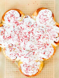 A large heart made out of cinnamon rolls, frosted in white and sprinkles on top.