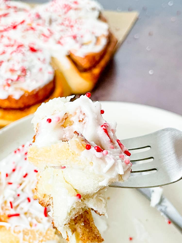A bite of a Valentine's Day Breakfast Cinnamon Roll. With frosting and sprinkles on a fork. 