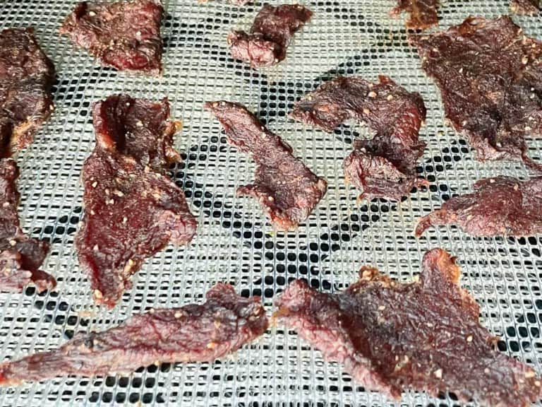 Slices of homemade beef jerky drying on a rack in a food dehydrator.