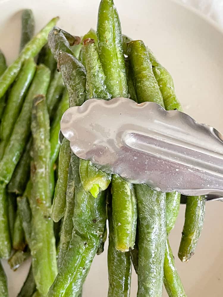 A serving of air fryer green beans in tongs.