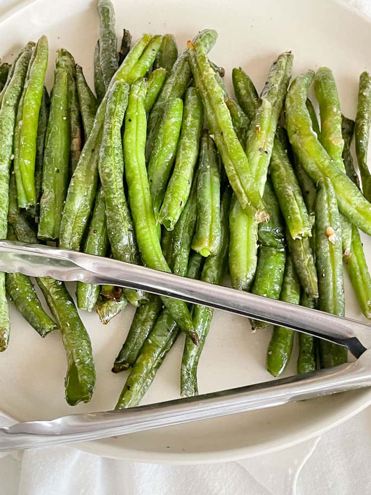 A plate of air fryer green beans with tongs for serving.