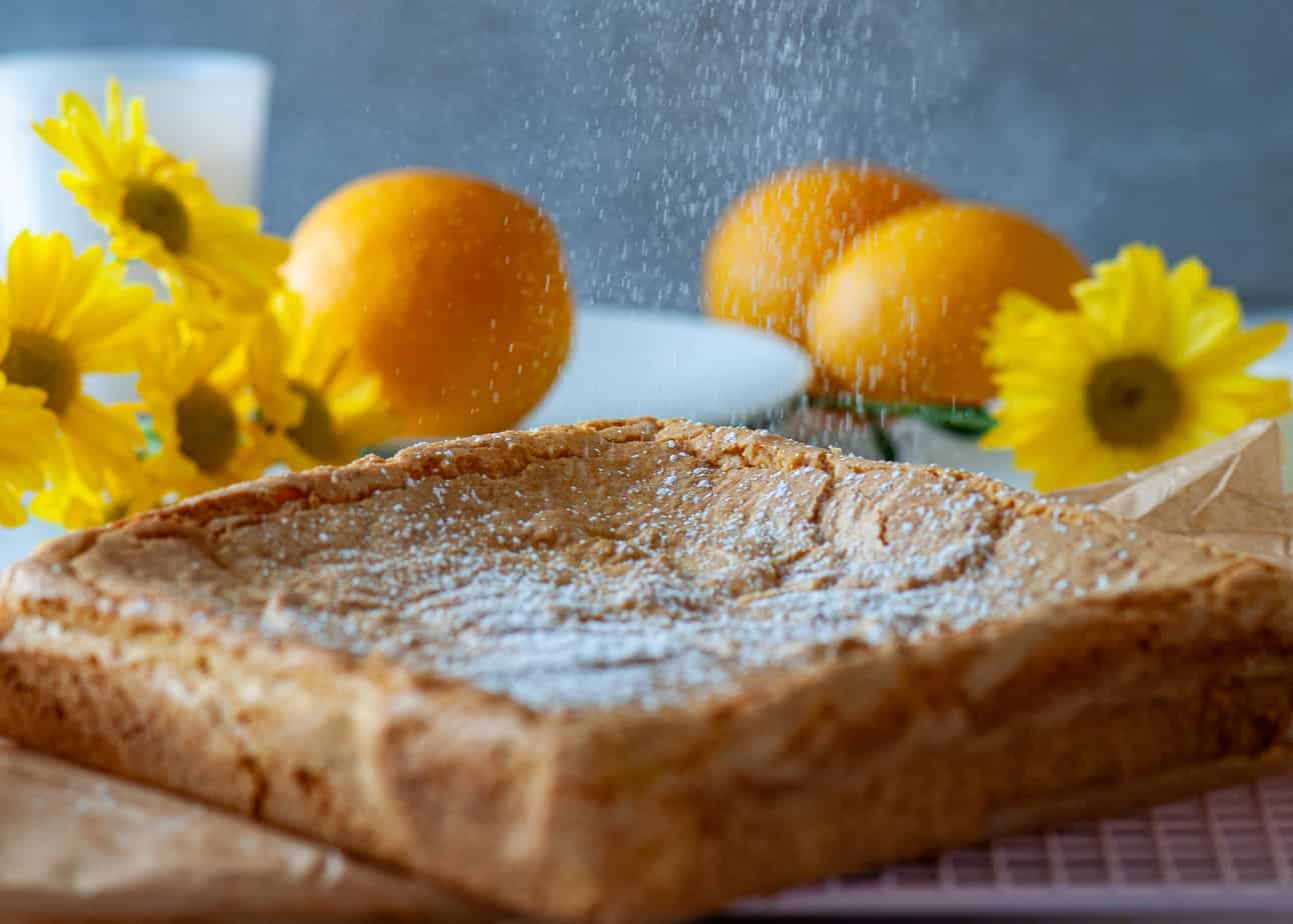 Lemon brownies on a cooling tray with sunflowers and oranges in the background.