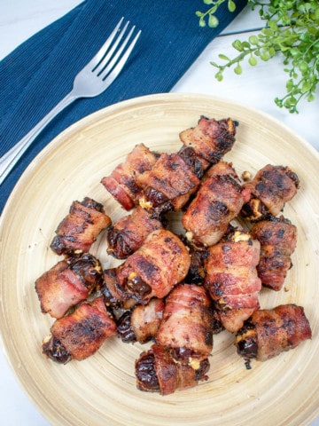 Featured photo for bacon wrapped dates. Dates on a plate with a fork and greenery.