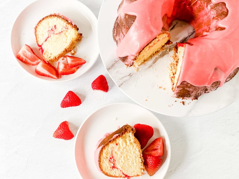 2 slices of strawberry pound cake with a cake and strawberries.