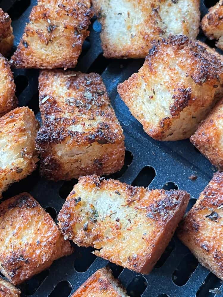 Close up of several fresh croutons in the air fryer basket.