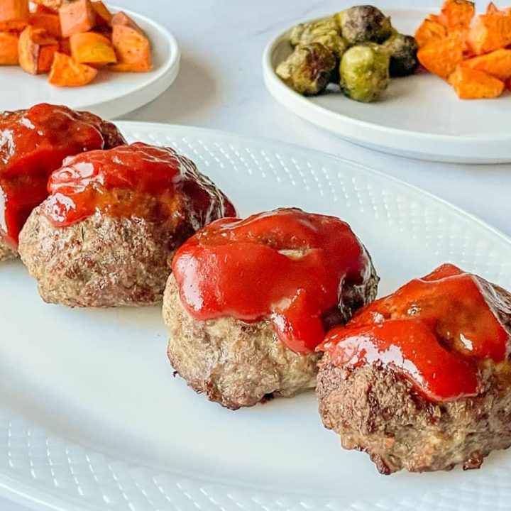 4 Mini Meatloaves on a platter with side dishes in the background.