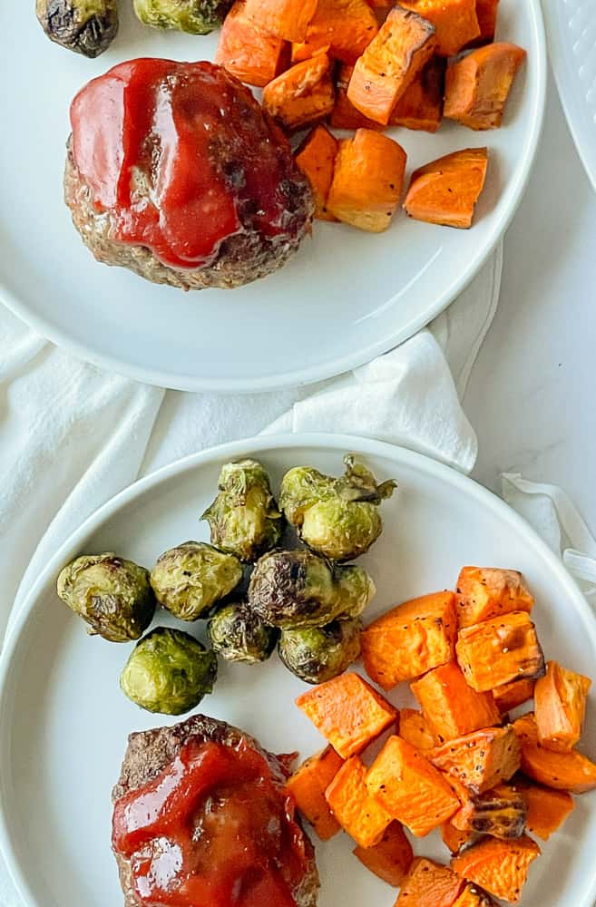 Two plates with mini meatloaves topped ketchup, roasted sweet potatoes, and Brussels sprouts.