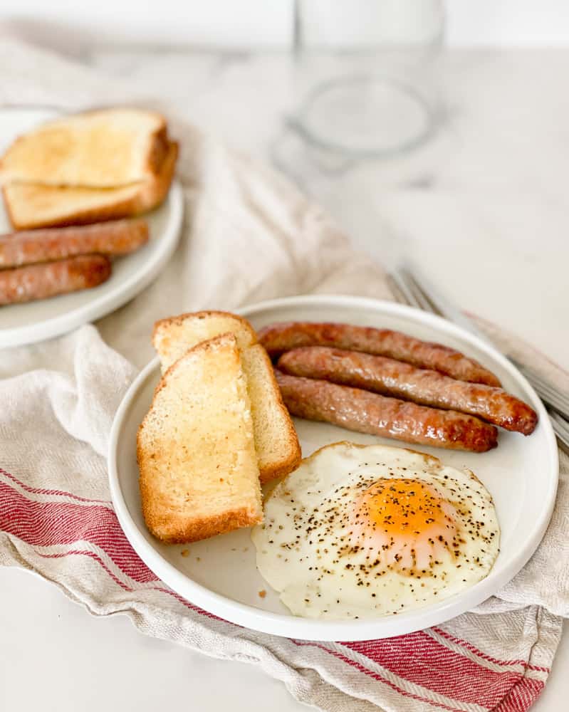 Breakfast for two with sausages, toast, and eggs, on plates.