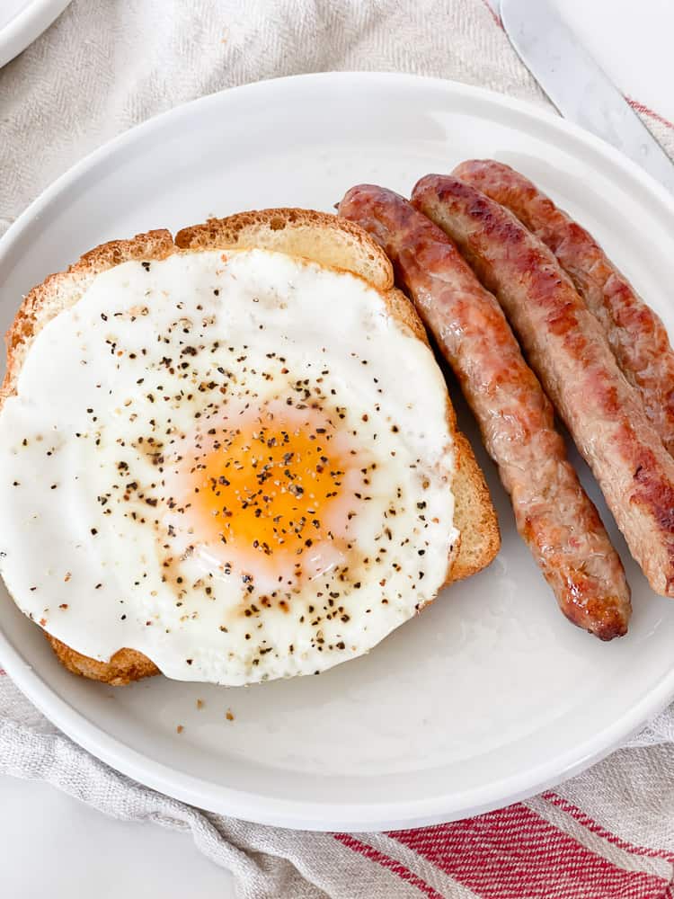 Egg, toast, sausage links on a white plate.