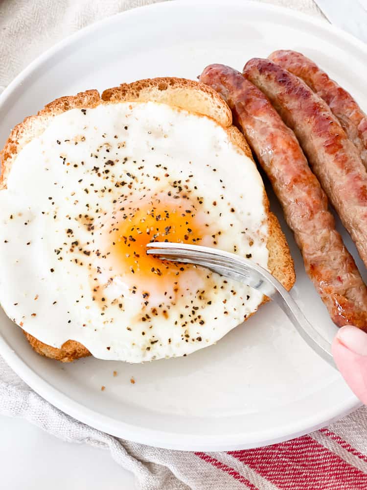Egg on toast with a fork and several fried sausages.