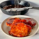 4 Steaming Oven BBQ Pork Chops on a plate with a cast iron frying pan.