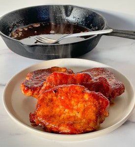 4 Steaming Oven BBQ Pork Chops on a plate with a cast iron frying pan.