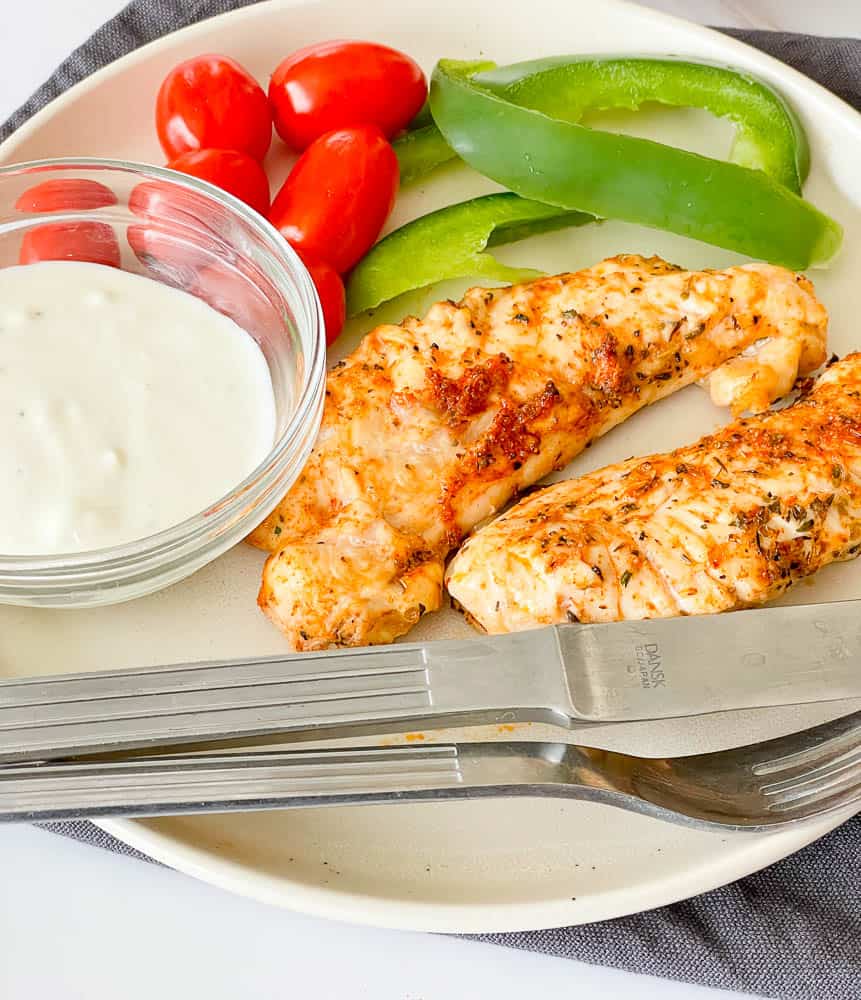 Air Fryer Chicken Tenders on a plate with dip, and fresh veggetables.