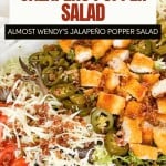 A close-up of a salad topped with jalapeños, cheese, diced breaded chicken, bacon bits, and shredded lettuce, inspired by the Wendy's Chicken Salad Recipe and labeled as copycat jalapeño popper salad.