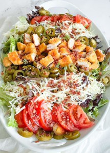 Vertical image of a Jalapeño Popper Salad. Lettuce, crispy chicken, tomatoes, bacon, colbyjack, and jalapeños.