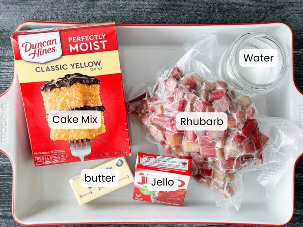 A tray with yellow cake mix, a stick of butter, a box of strawberry Jello, a bowl of water, and a bag of frozen rhubarb&mdash;perfect ingredients for making a classic Rhubarb Dump Cake&mdash;all clearly labeled.