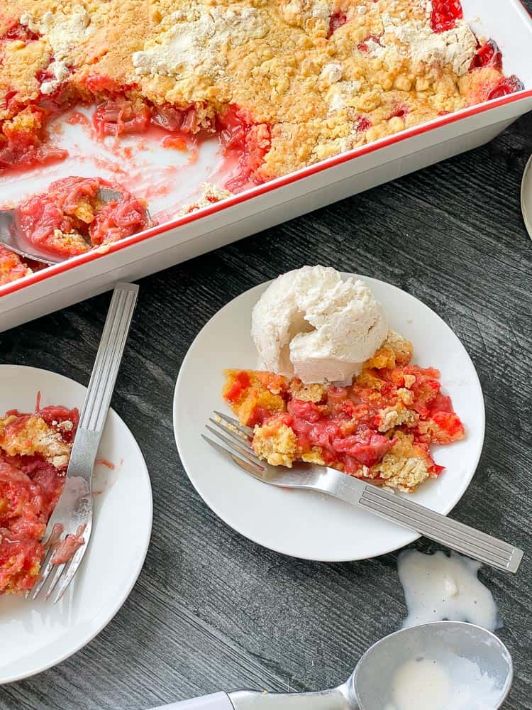 Rhubarb Dump Cake in pan with two plates of cake and a scoop of ice cream.
