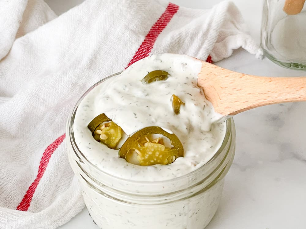 A spoon in a jar of jalapeño ranch dressing.