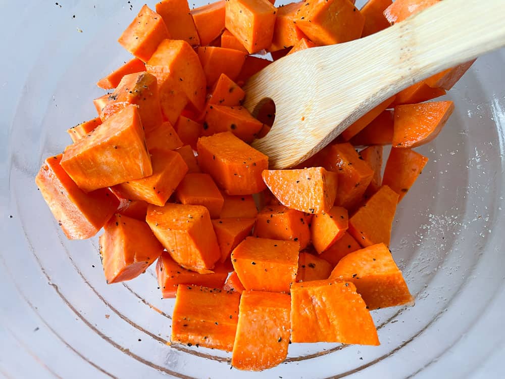 Chopped sweet potatoes with oil, salt, and pepper in a bowl.