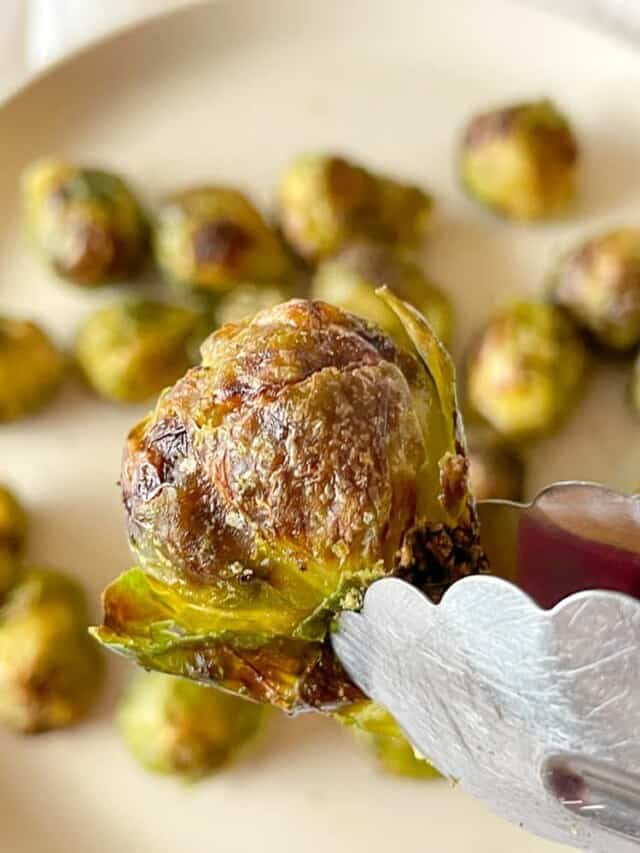 Brussel Sprout perfection, one sprout in a pair of tongs with more sprouts behind it on a plate.