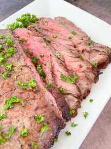 London Broil with parsley on a white plate.