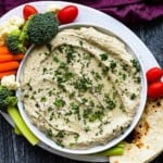 Babaganoush surrounded by vegetables and topped with parsley.