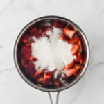 Adding sugar to the sliced strawberries for the strawberry puree.