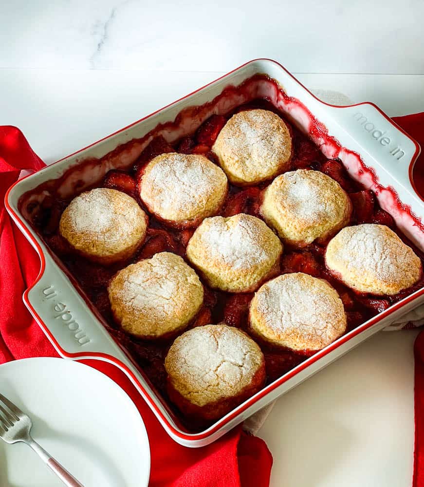 fresh biscuit topped dessert in a pan with plates, forks and napkins.