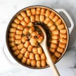 A casserole of tater tot with a ladle scooping some of it.